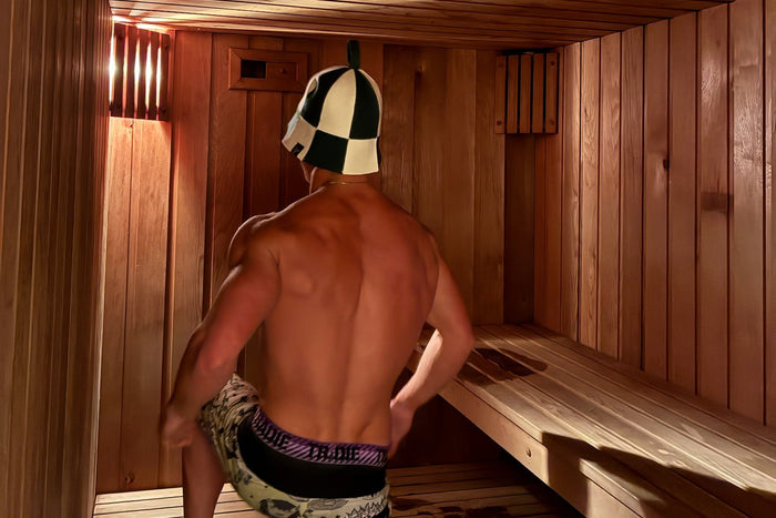A premium lifestyle photo with a muscular man wearing a Koala sauna hat in a modern timber sauna, clean minimal wellness aesthetic, realistic photography, no text.