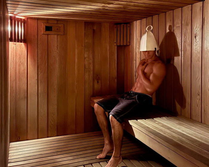 Person wearing a green and cream natural sauna hat inside a timber sauna.