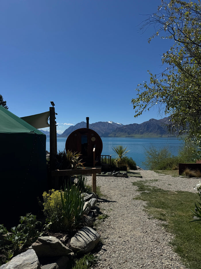 Wood-fired barrel sauna beside Lake Hāwea with mountains in the background, The Secret Sauna near Wānaka