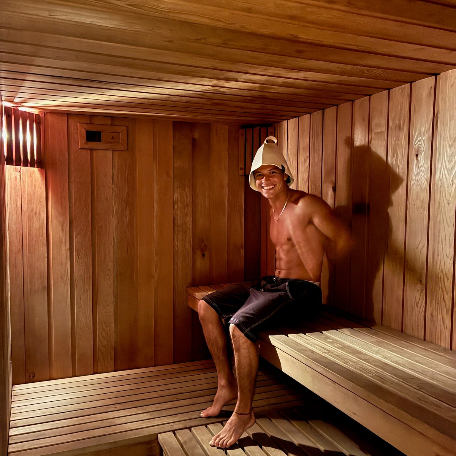 Athletic man resting on a wooden sauna bench while wearing a Koala merino wool sauna hat, designed to reduce heat stress on the head, protect hair and scalp, and help users stay in the sauna longer with greater comfort and recovery benefits.