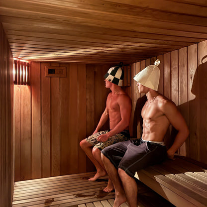 Two men sitting inside a traditional timber sauna wearing Koala wool sauna hats, demonstrating how sauna hats help regulate head temperature, reduce heat stress, and protect the scalp during high-heat sauna sessions for longer, more comfortable recovery.