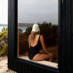 Woman wearing a Koala wool sauna hat while sitting inside a sauna by a large window, showcasing a premium wool sauna hat that helps regulate head temperature, reduce heat stress, and protect hair during longer, more comfortable sauna sessions.